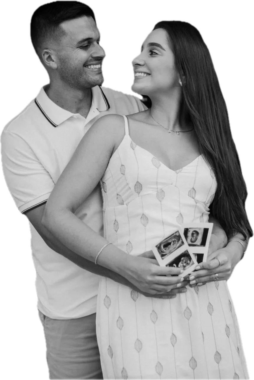 A couple smiling at each other, holding their baby's ultrasound photos